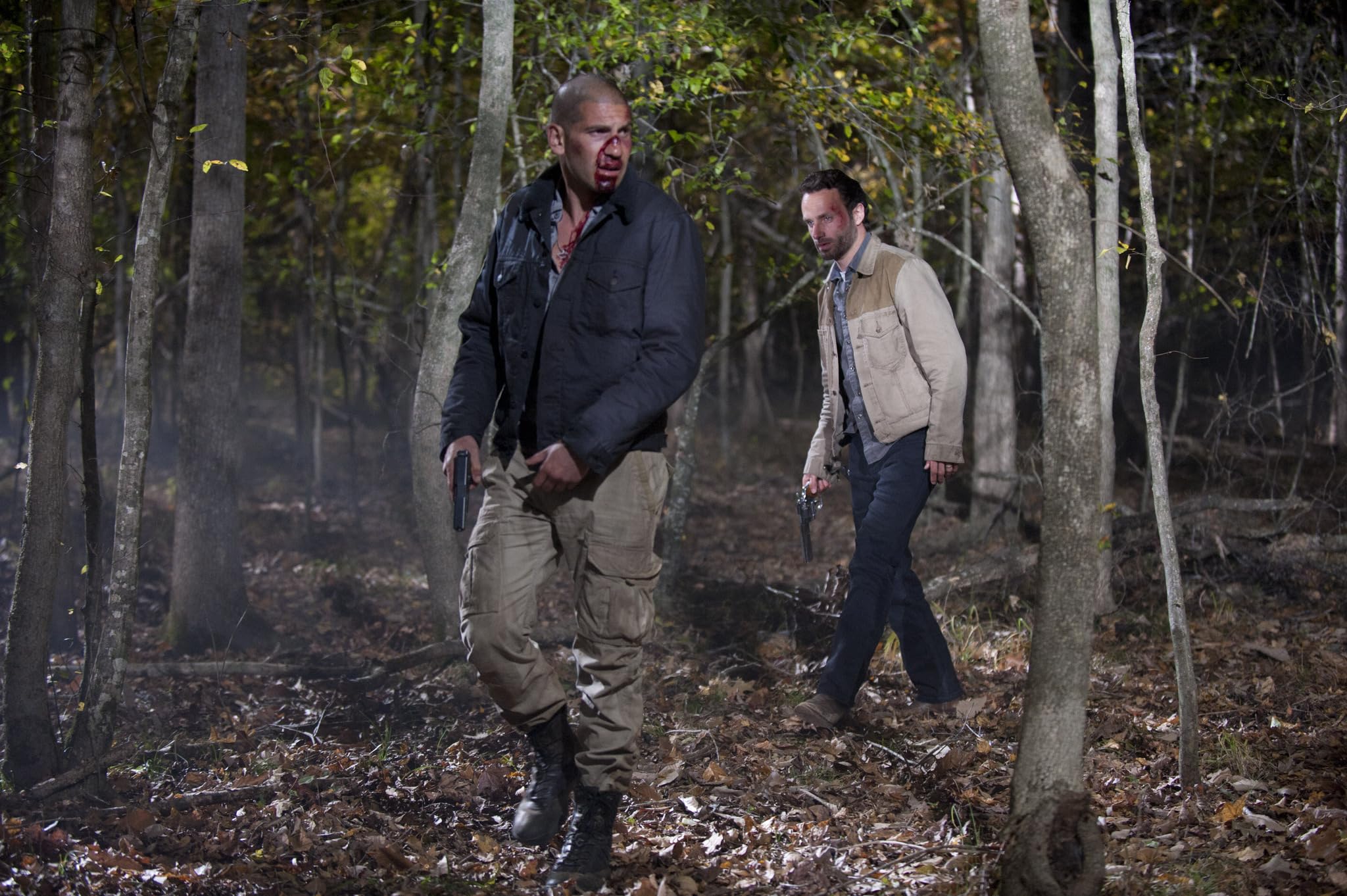 Shane Walsh (Jon Bernthal) and Rick Grimes (Andrew Lincoln) walk through the woods at night, guns in hand, in a still from The Walking Dead season 2 episode “Better Angels”